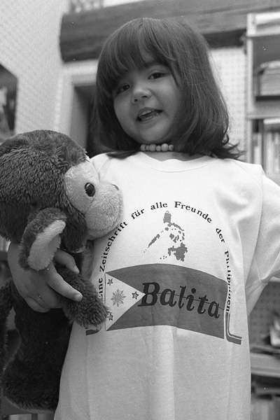 Mädchen mit Plüsch-Affe im Arm und T-Shirt mit Aufdruck "Balita".